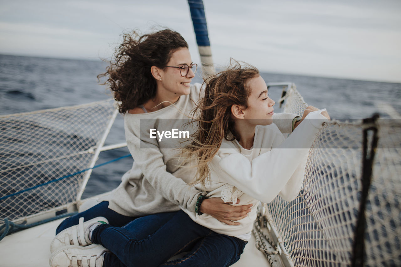 Mother and daughter looking at view while traveling through sailboat in sea during vacation