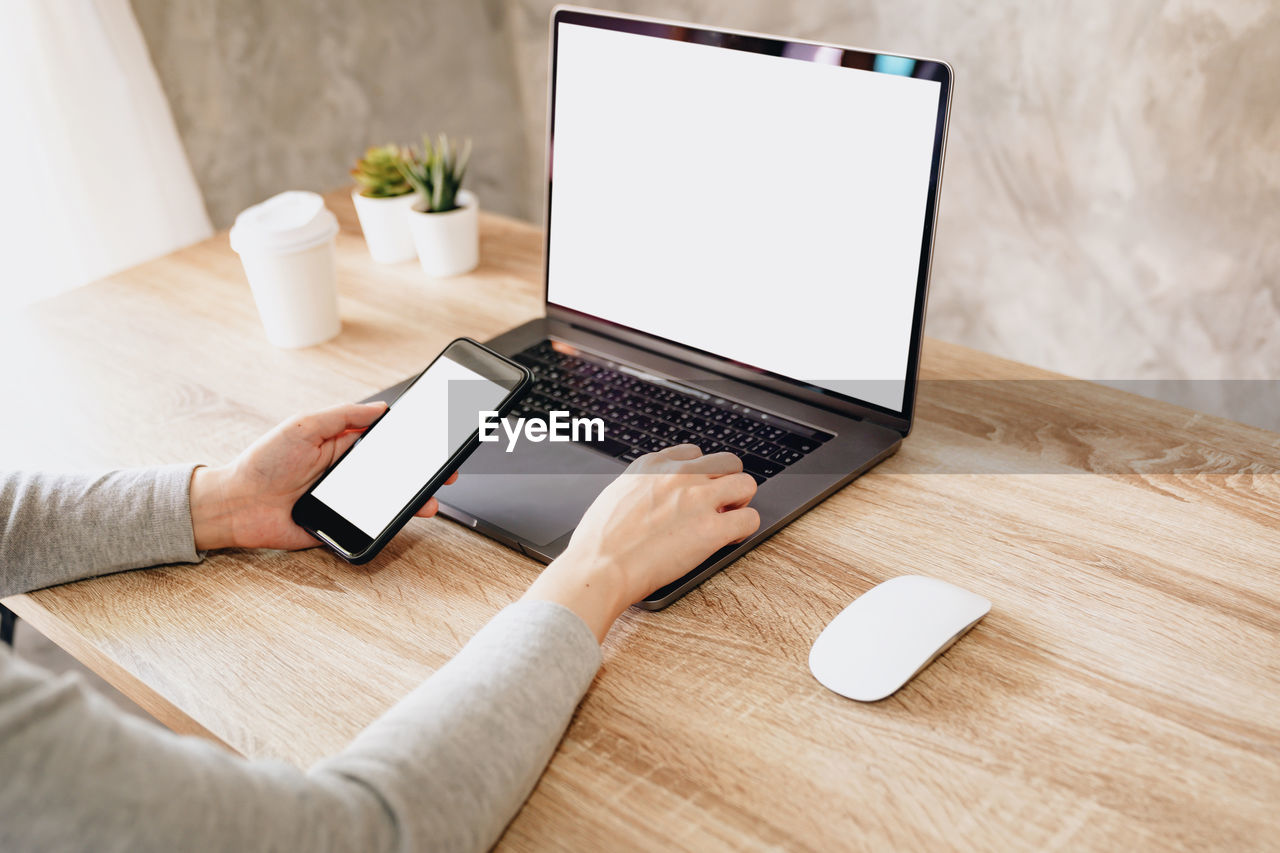 MIDSECTION OF PERSON USING LAPTOP ON TABLE