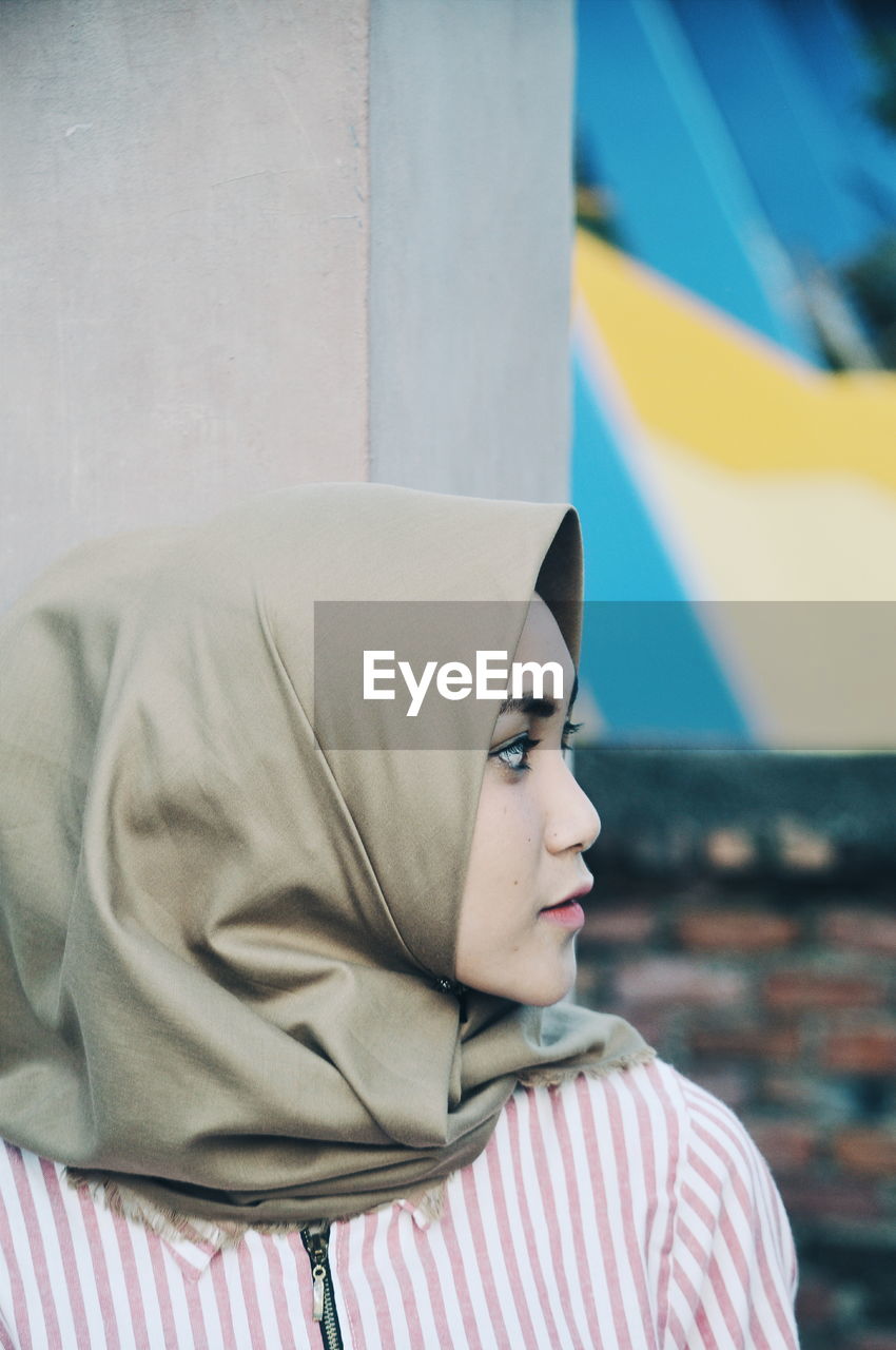 Woman wearing hijab while standing by wall