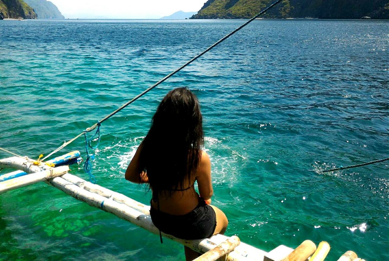 Rear view of young woman sitting on boat at sea