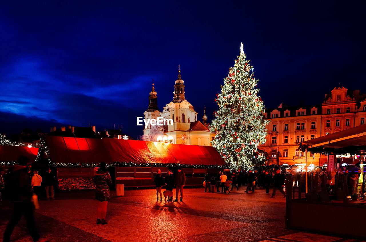 People celebrating christmas by illuminated buildings at night