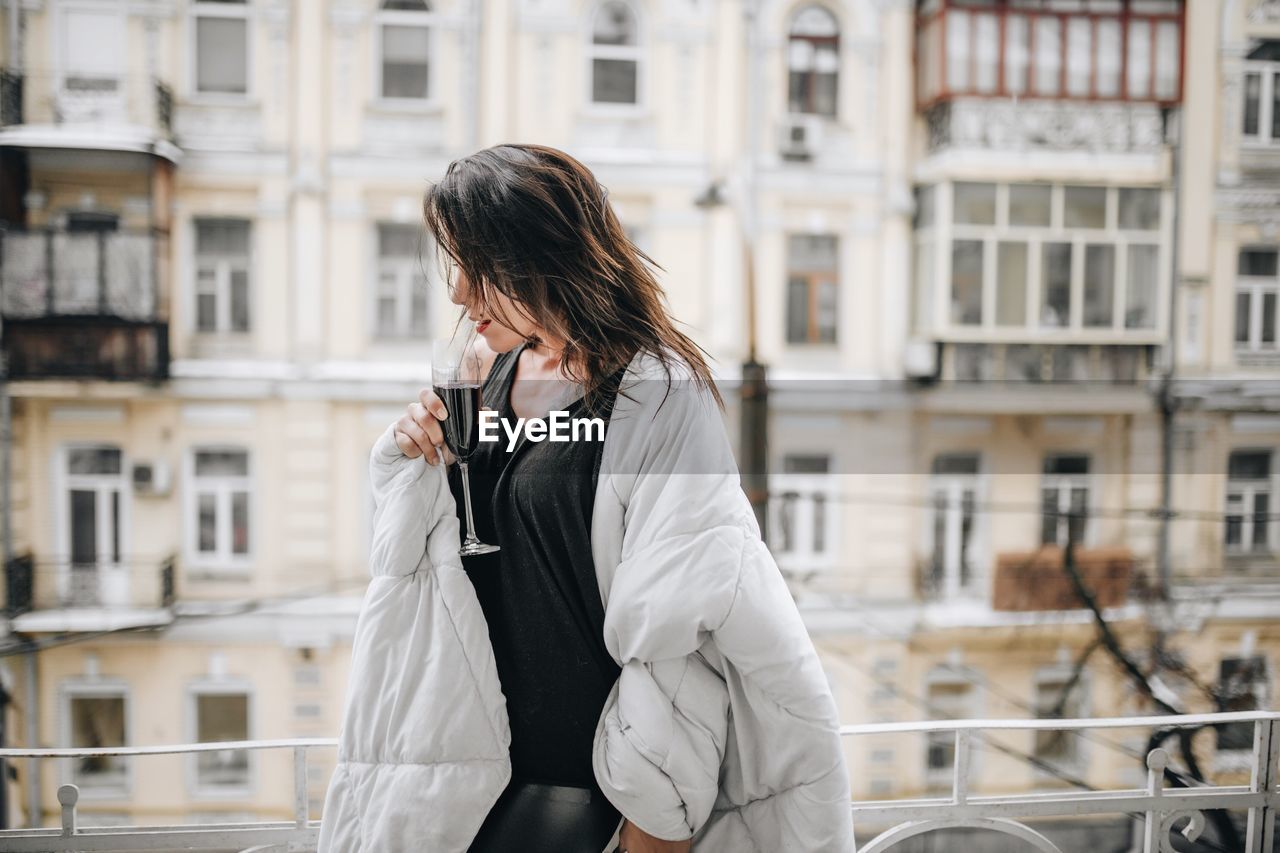 Woman having red wine while wrapped in blanket at balcony