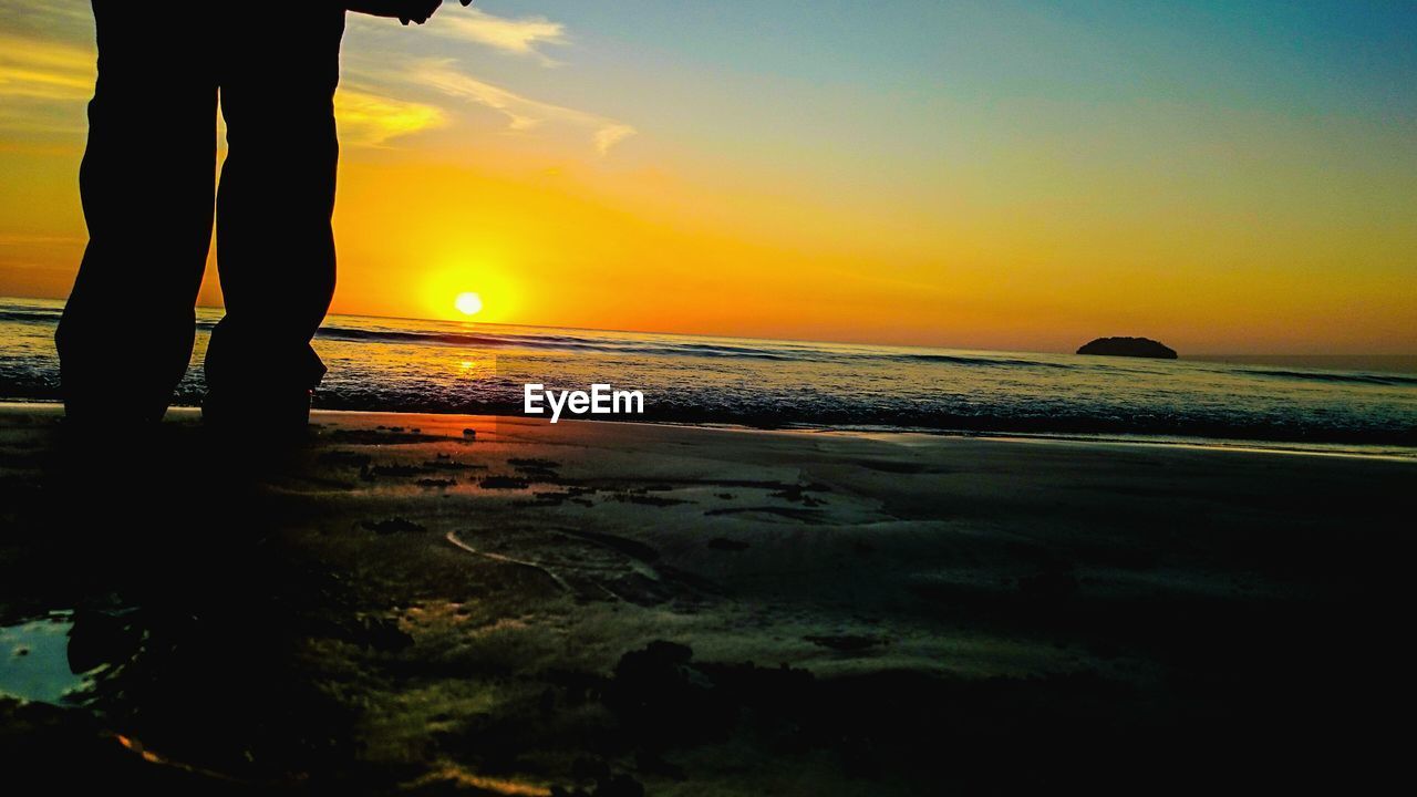 LOW SECTION OF SILHOUETTE MAN ON BEACH AT SUNSET