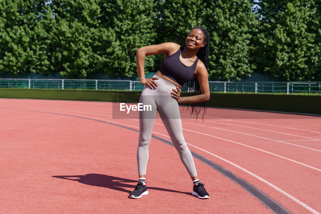 Young african american woman fitness trainer demonstrating warm-up exercises standing on stadium