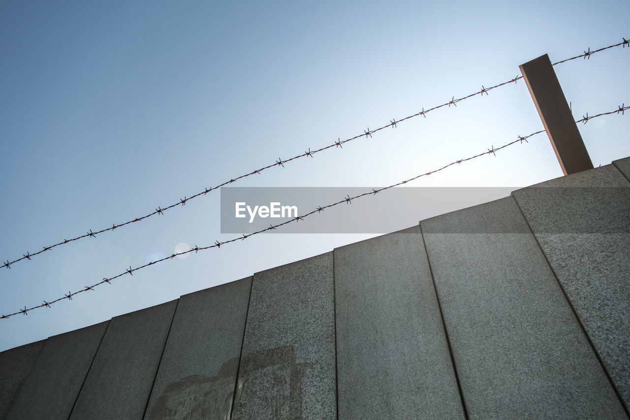 Low angle view of barbed wire over wall against clear sky