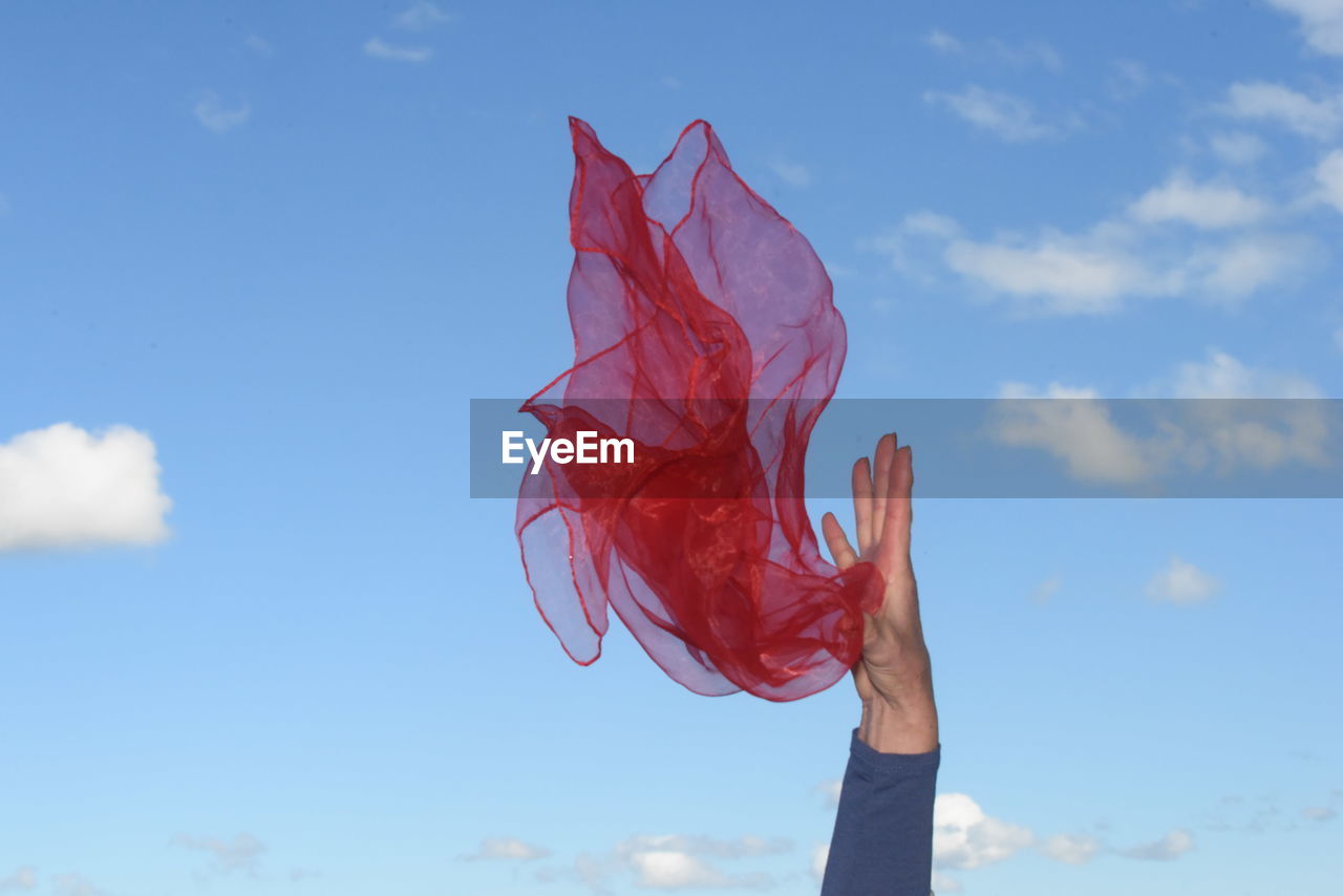 Low angle view of person holding textile against blue sky