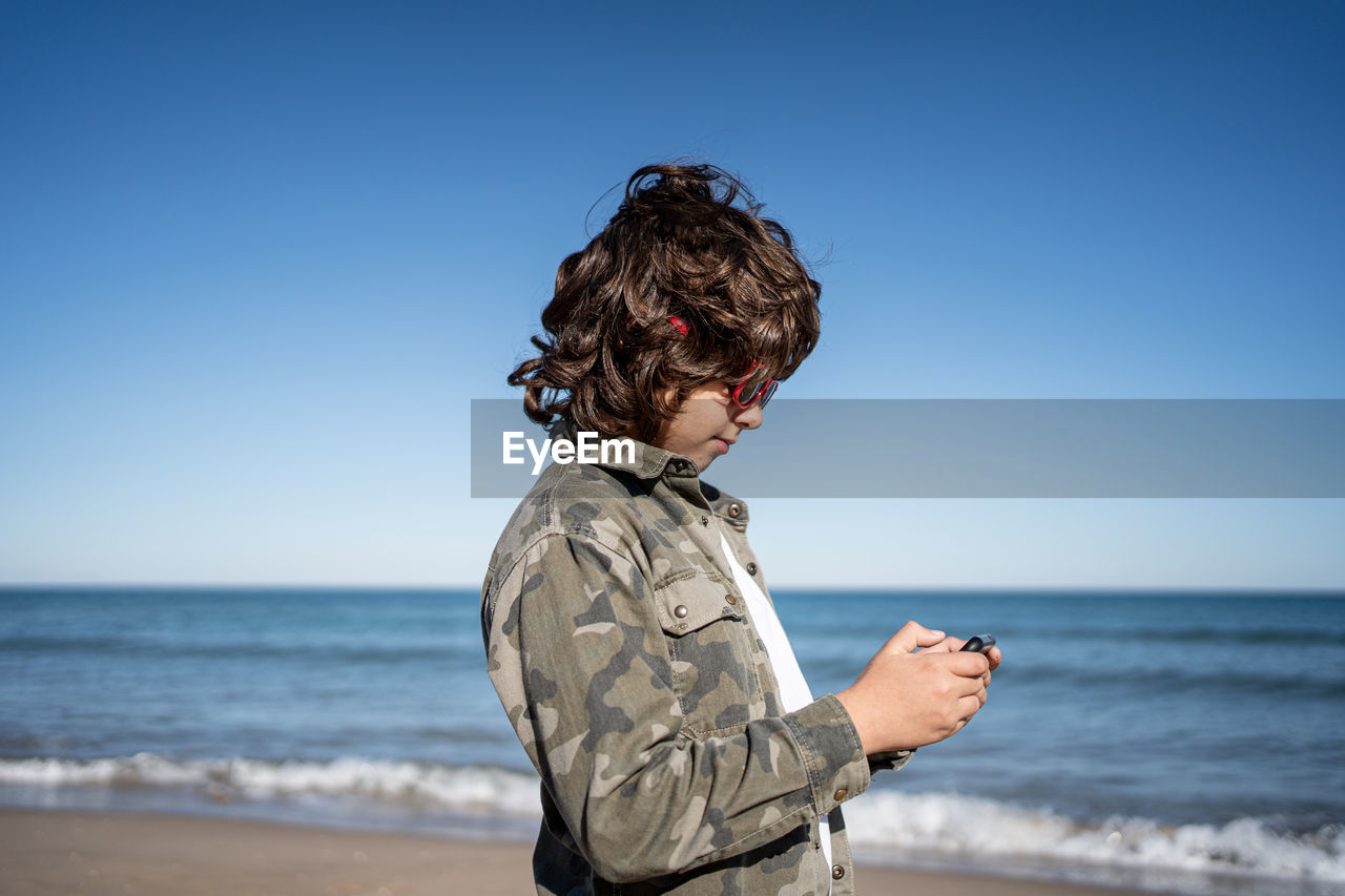 Boy with sunglasses on the beach playing with a mobile on a sunny winter day