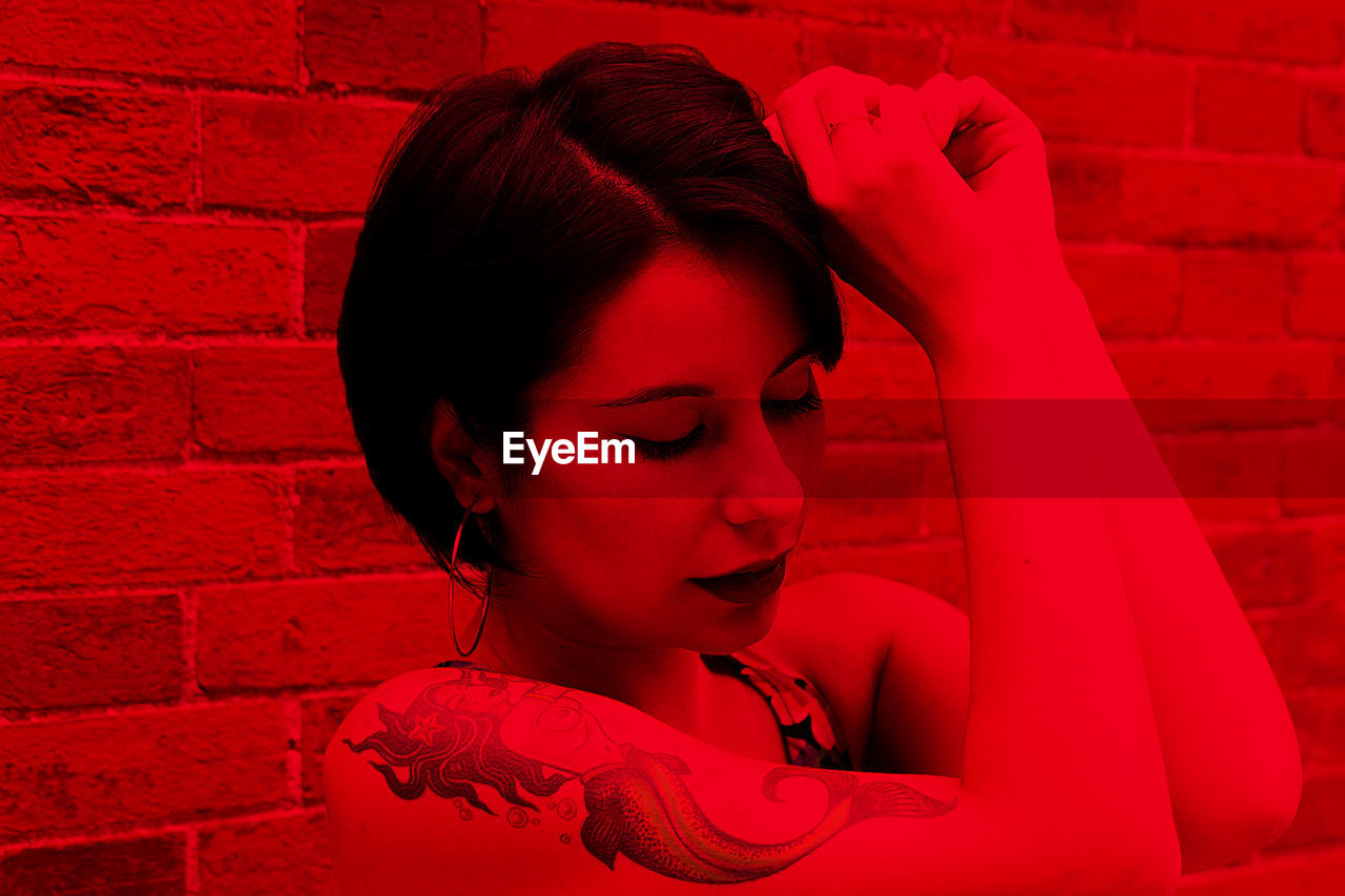 Young woman with tattoos posing against wall with red color