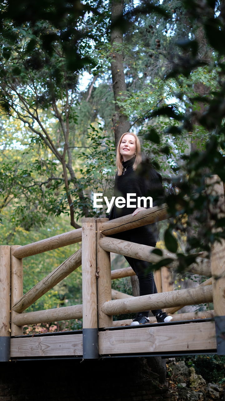 Low angle portrait of young woman standing on wooden bridge