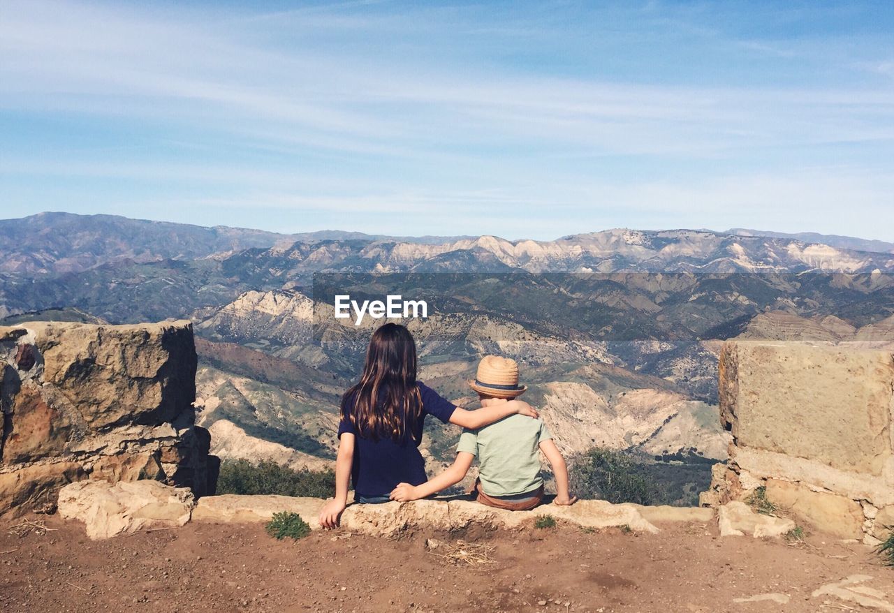 Rear view of siblings sitting against landscape