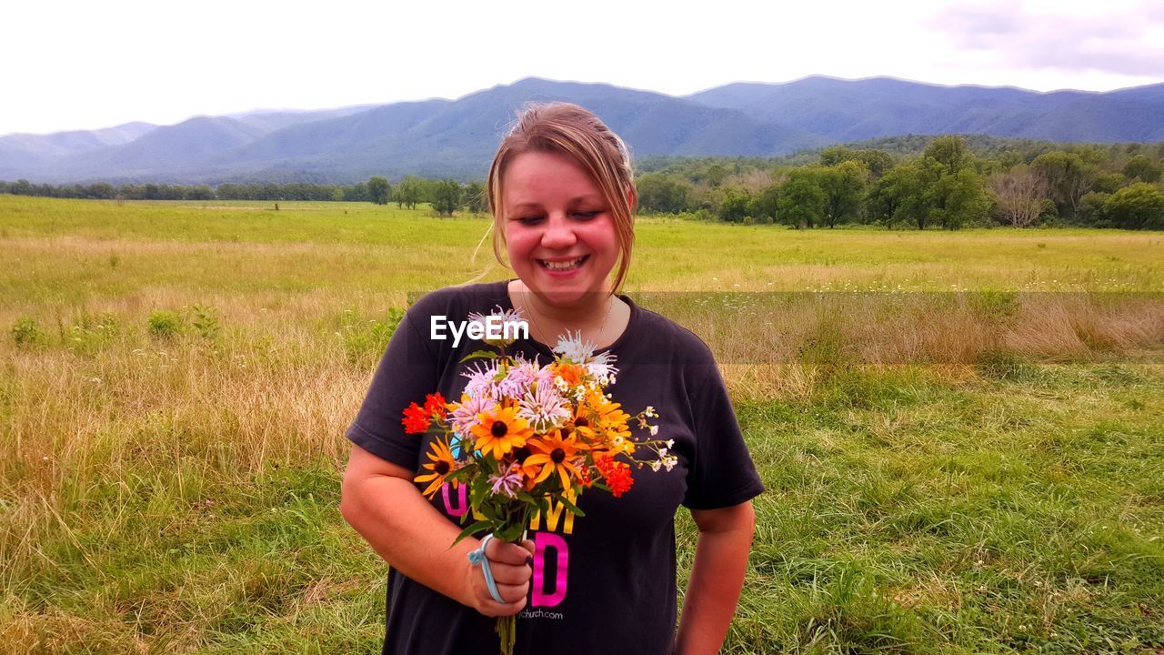 BEAUTIFUL YOUNG WOMAN STANDING BY FLOWER FIELD