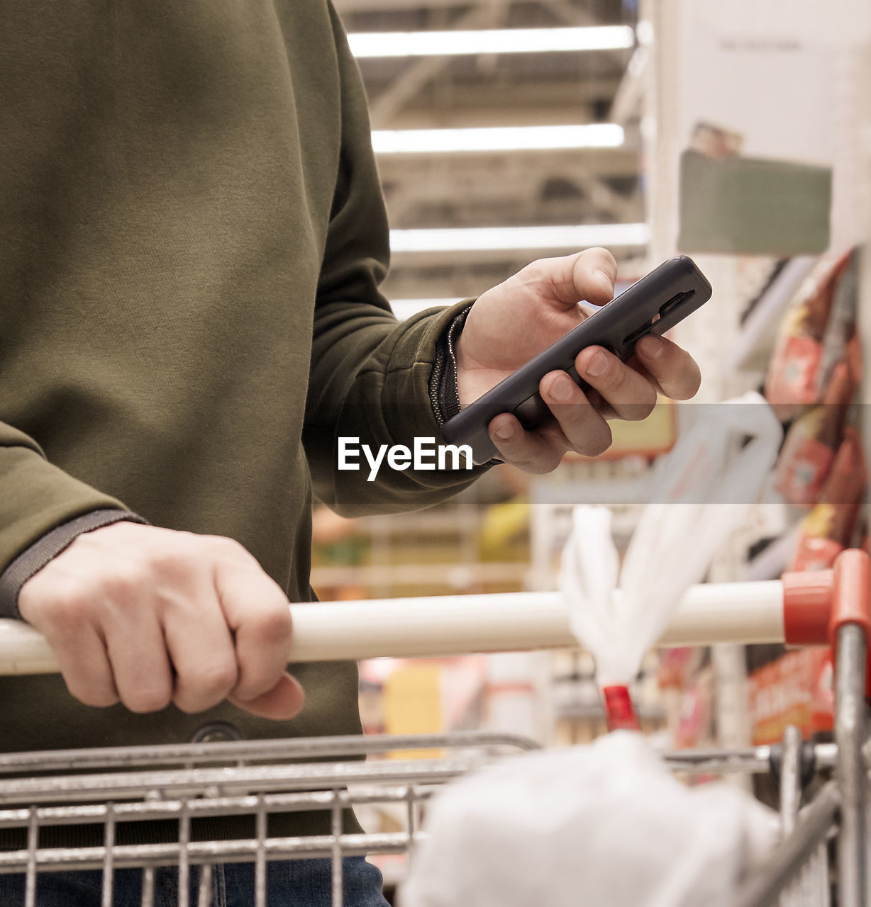 Midsection of man using mobile phone while shopping