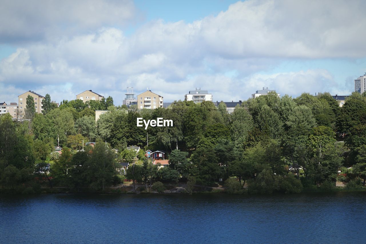 View of trees by river against cloudy sky