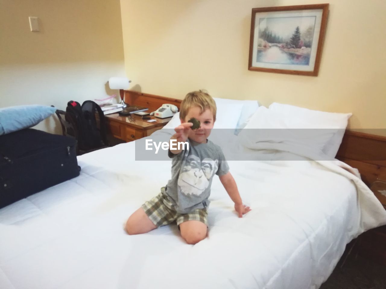 Boy holding toy while kneeling on bed at home