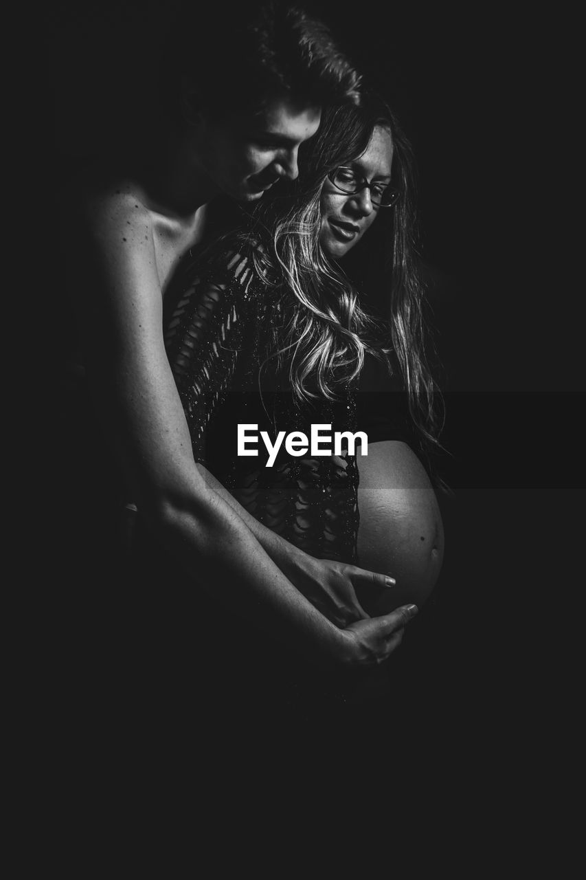 Young man with pregnant woman against black background