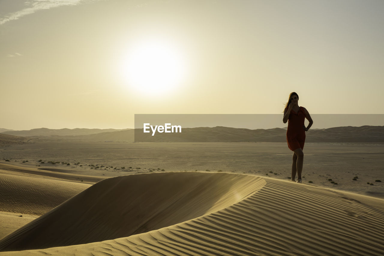 Woman standing at desert against clear sky