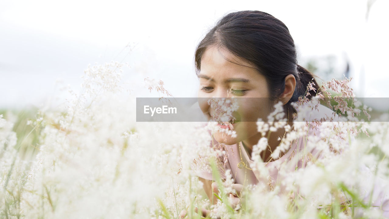 Close-up of young woman looking at flowers against sky