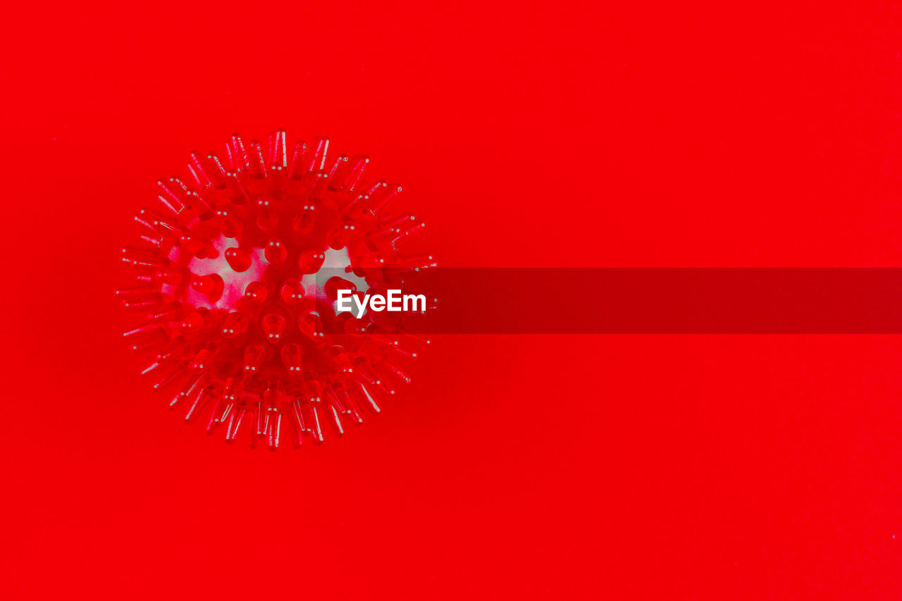 Red medical massager in the form of a ball with spikes on a red background with a copy space