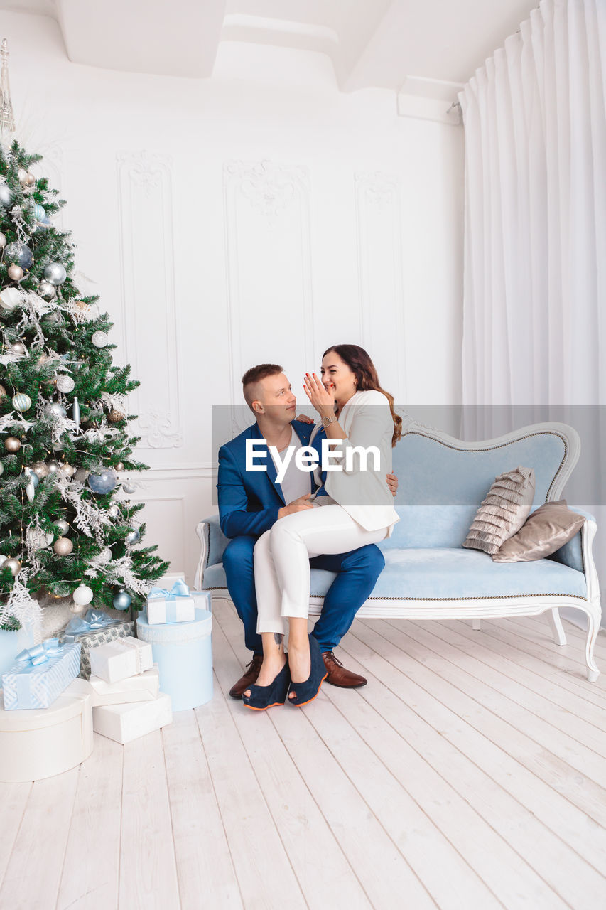 Couple sitting on sofa by christmas tree at home