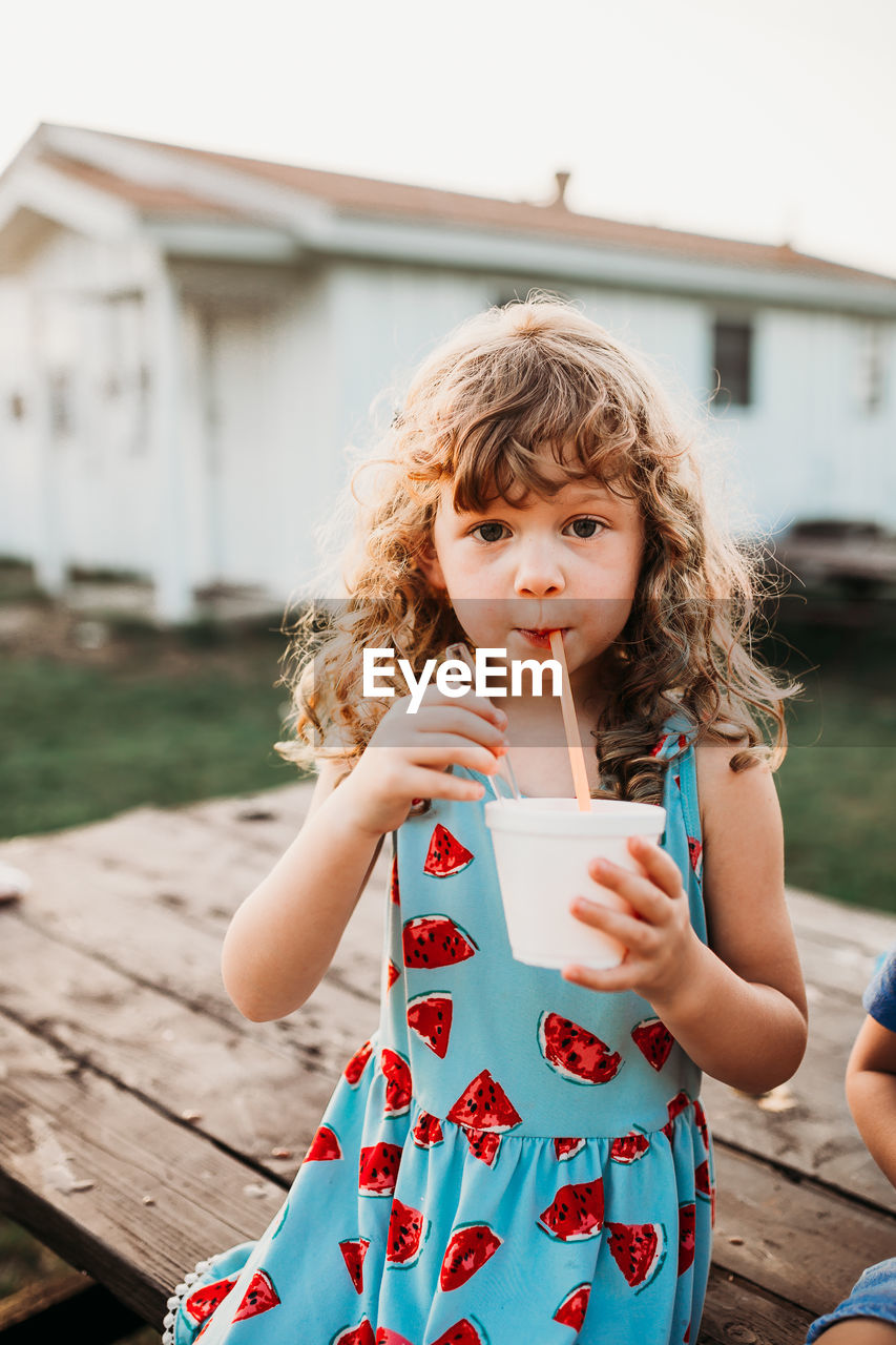 Close up of young girl drinking snow cone at table during sunset