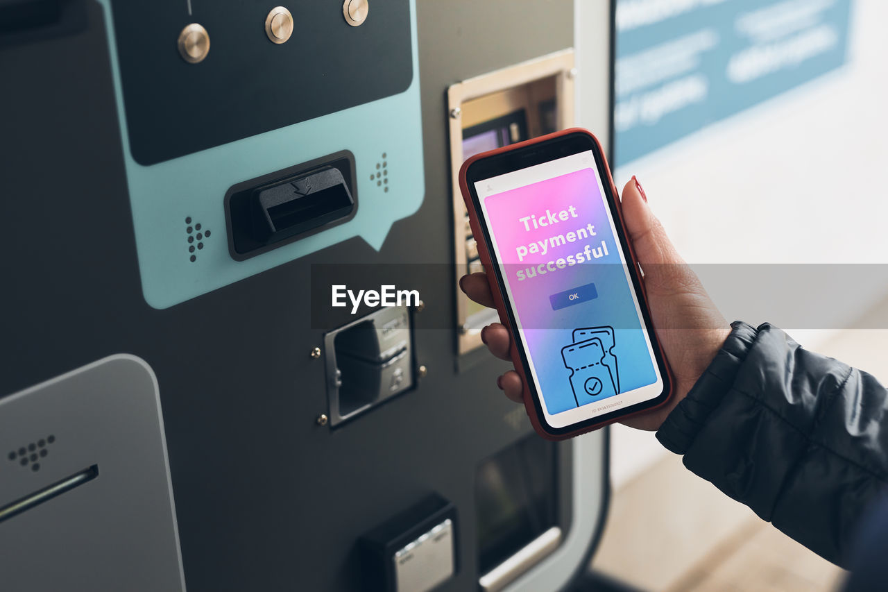 Woman buying ticket at ticket machine paying using payment app on smartphone. using technology