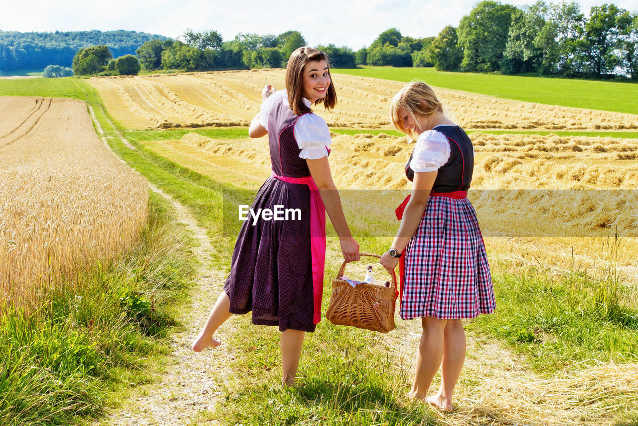 Portrait of young woman with friend holding basket on field