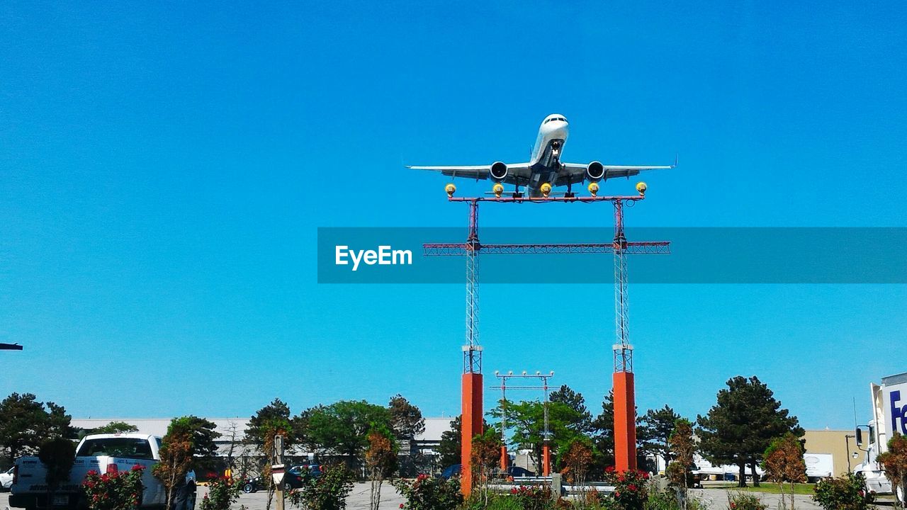 Airplane above floodlight against clear blue sky