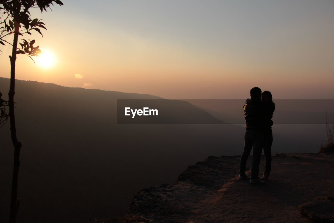 Couple standing on mountain against sky during sunset