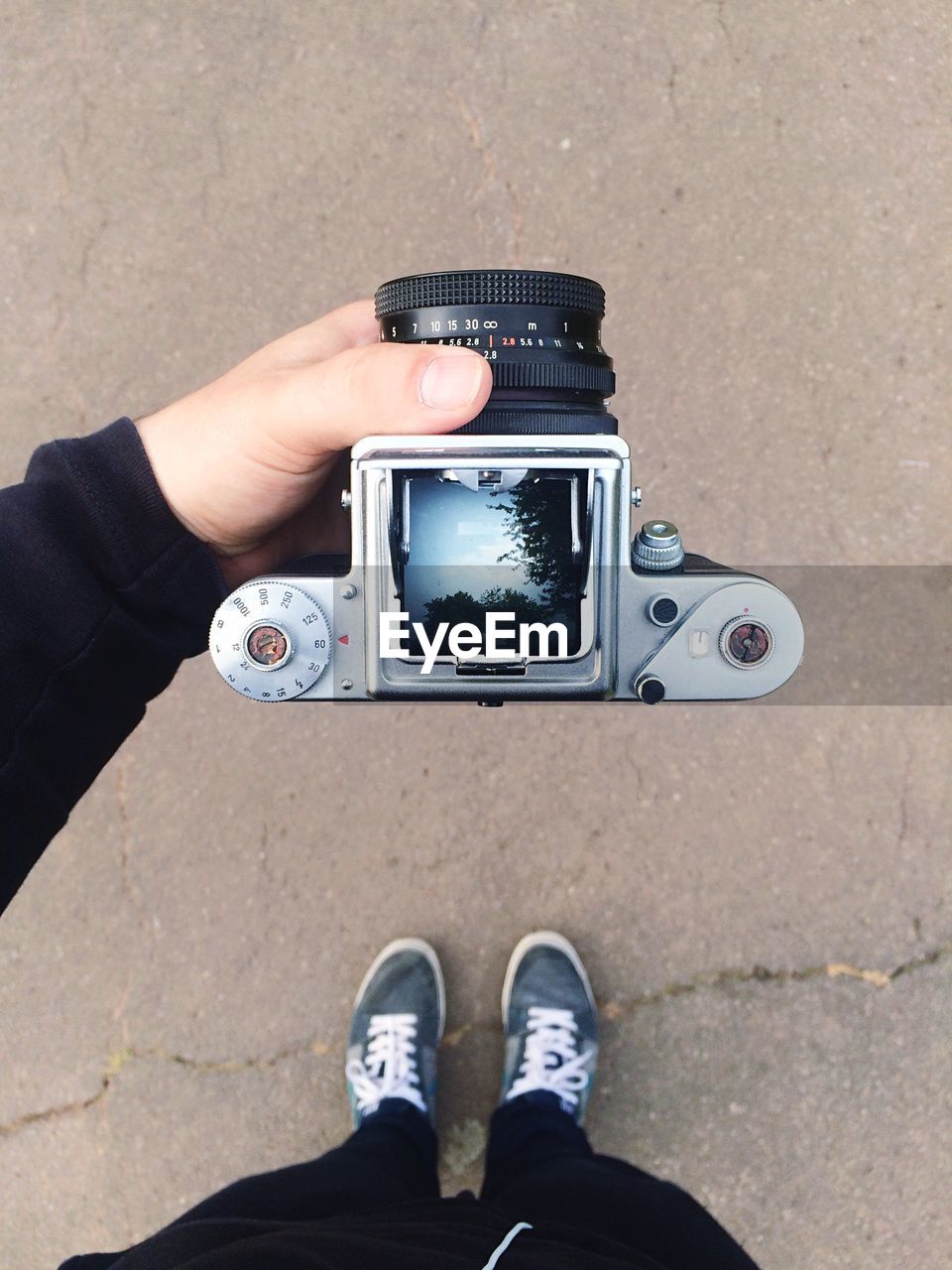 High angle view of man holding camera with reflection of tree in