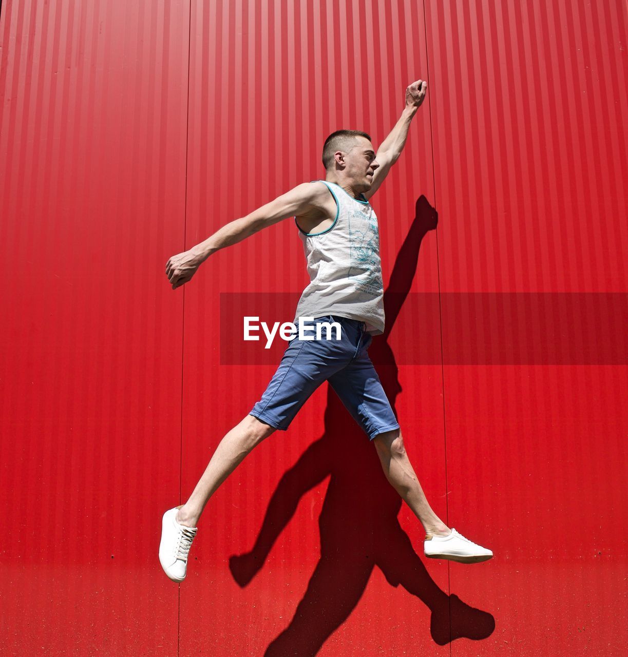 Full length of man jumping against red wall
