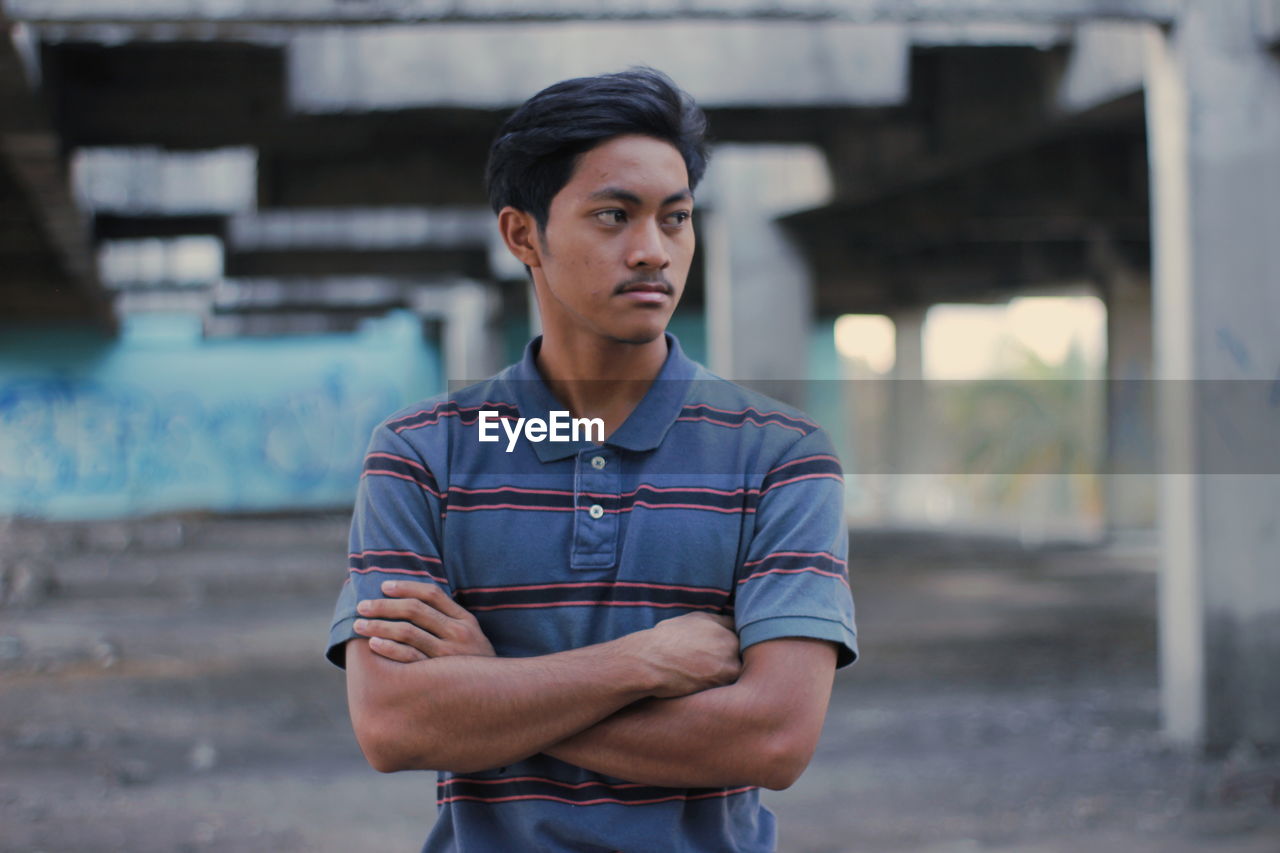 Man looking away while standing with arms crossed