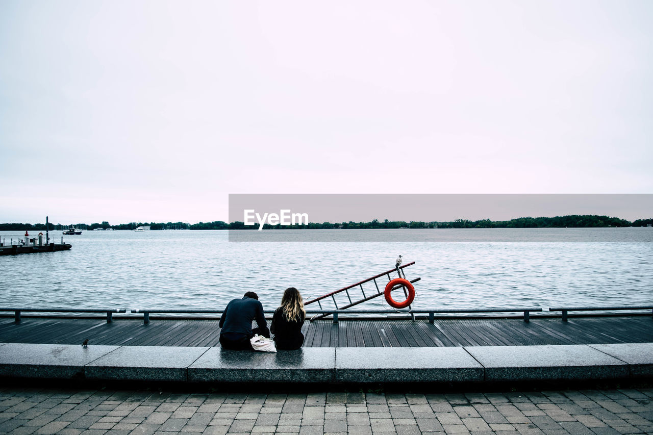 MEN SITTING ON BOAT AGAINST LAKE