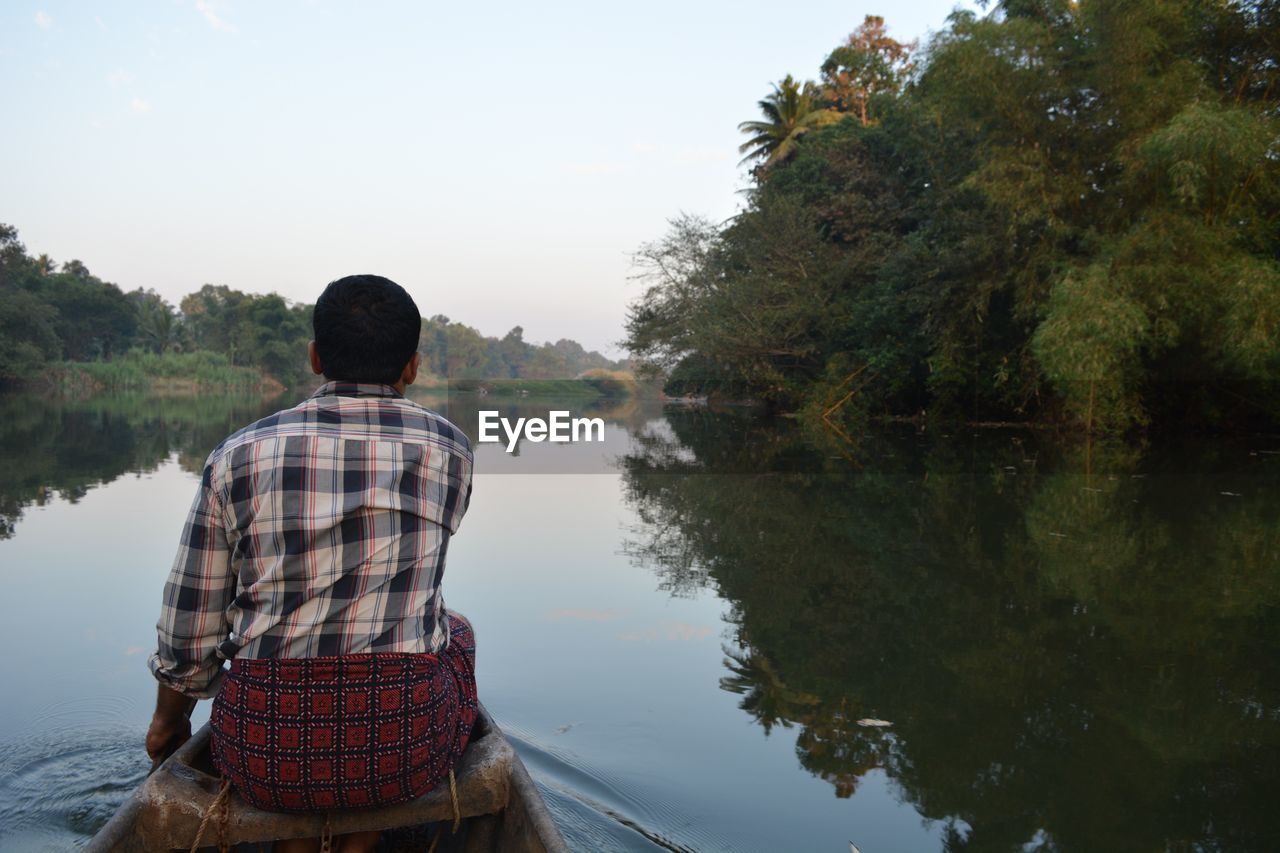 REAR VIEW OF MAN STANDING IN LAKE AGAINST SKY