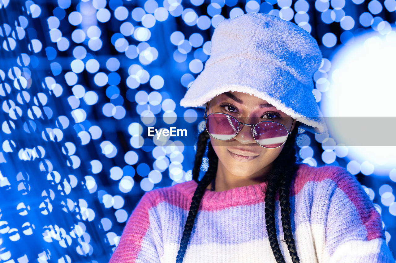Joyful woman of color with a white beanie braided hairstyle and pink glasses enjoying the christmas