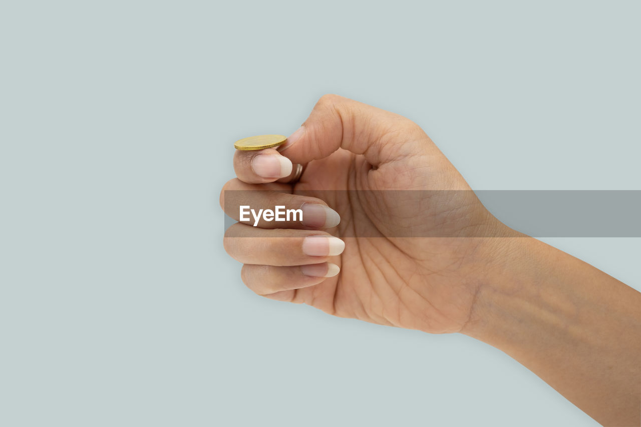 Cropped hand of woman holding coin against gray background