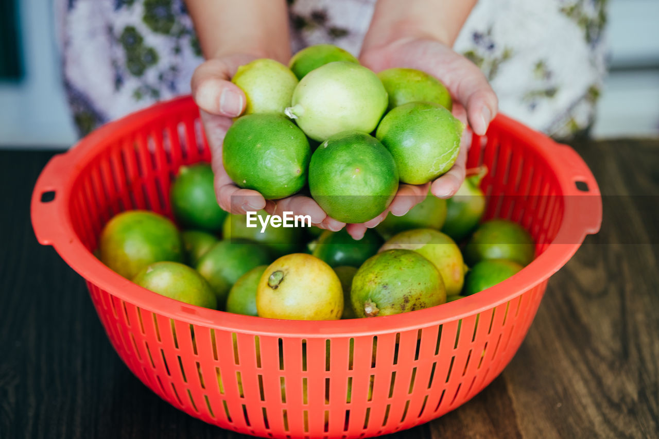 Midsection of person holding lime in basket on table