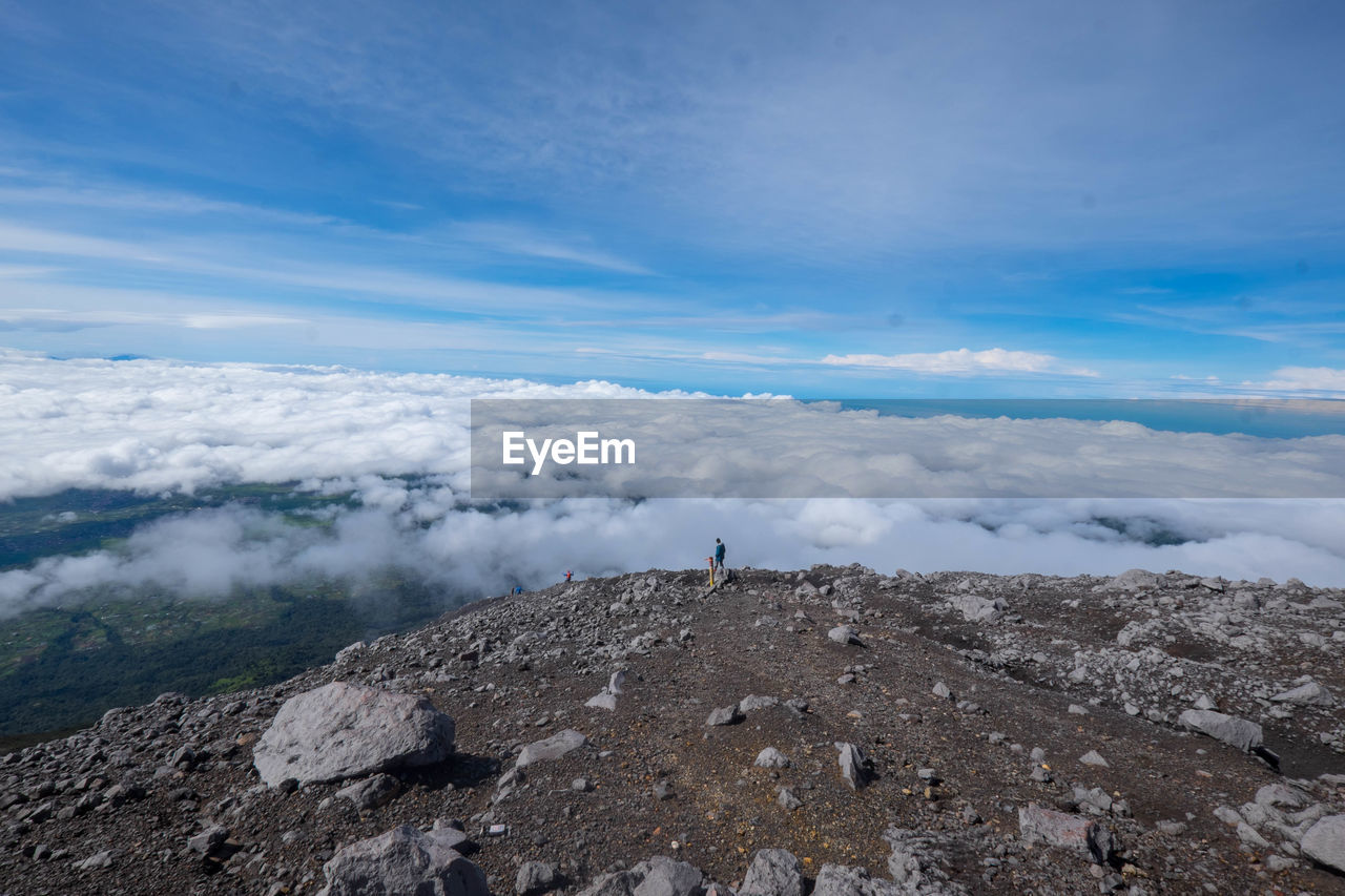 Mid distance view of man standing on cliff against cloudy sky
