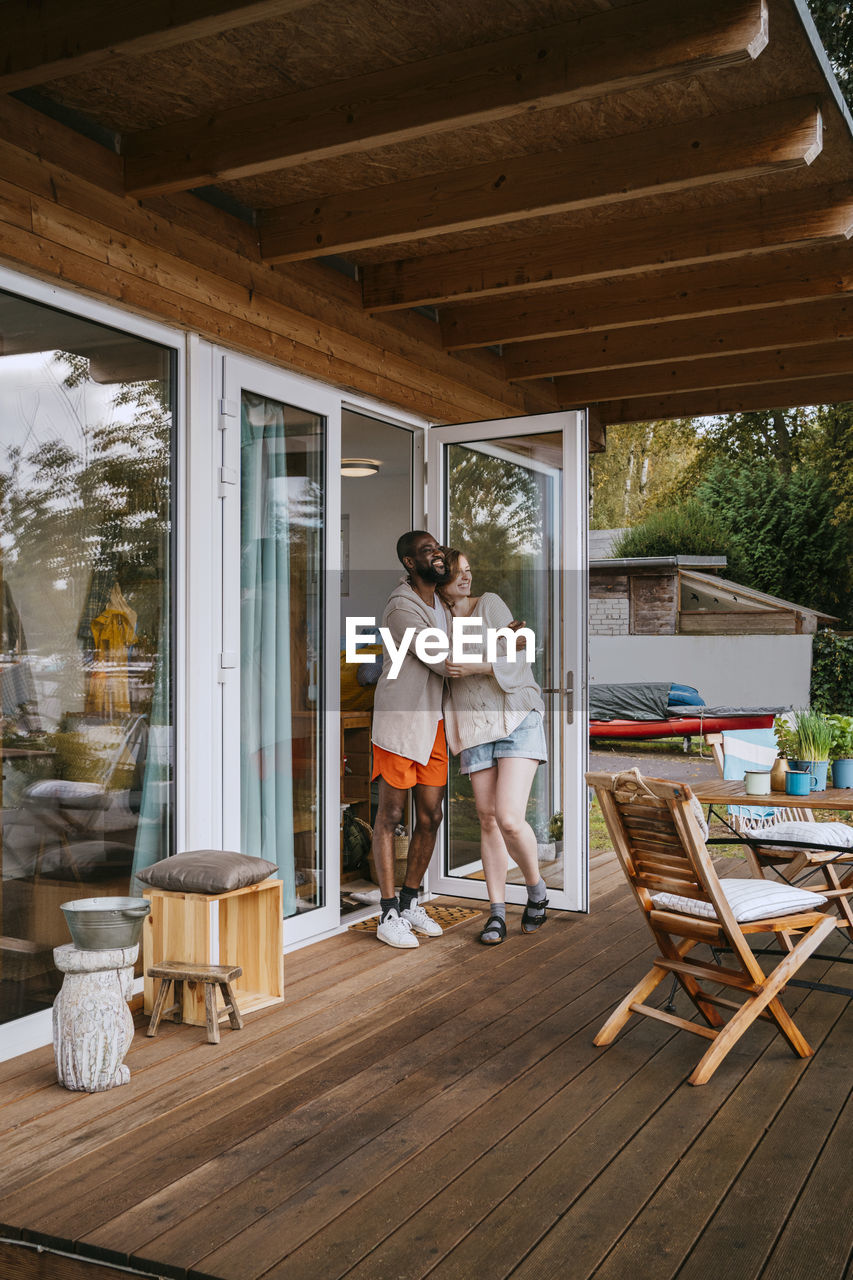 Multiracial couple embracing each other while standing on porch near doorway