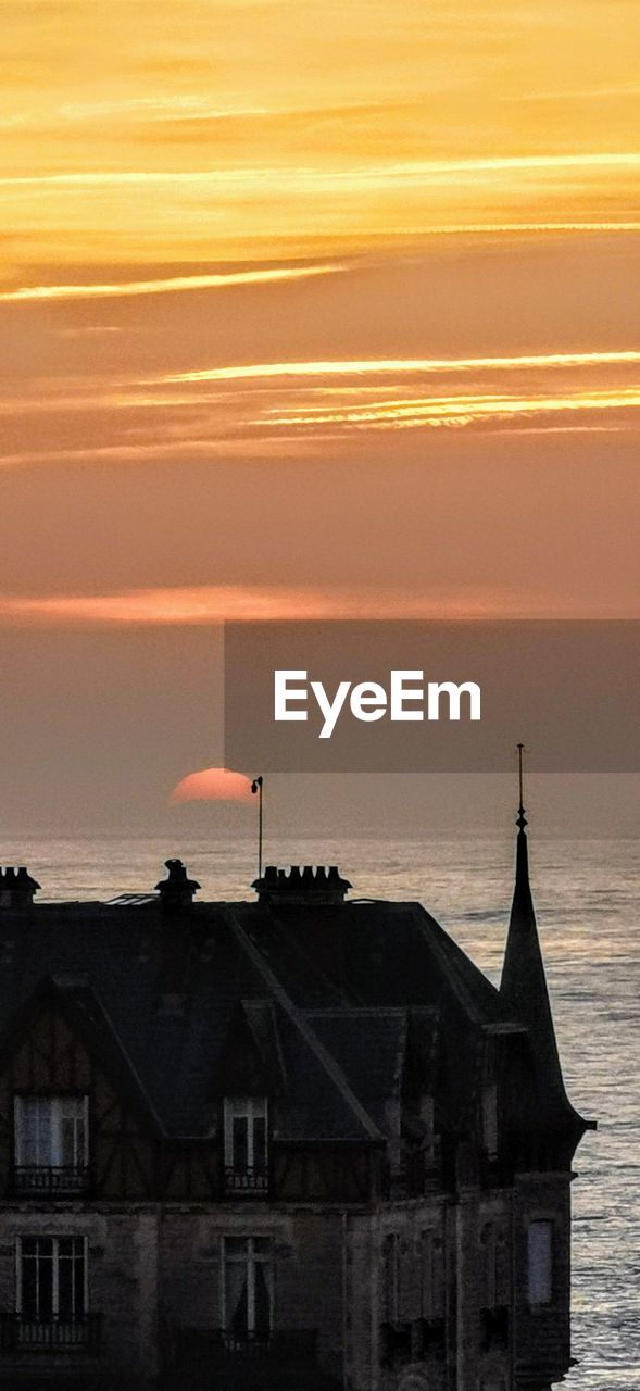 SILHOUETTE BUILDING BY SEA AGAINST SKY DURING SUNSET