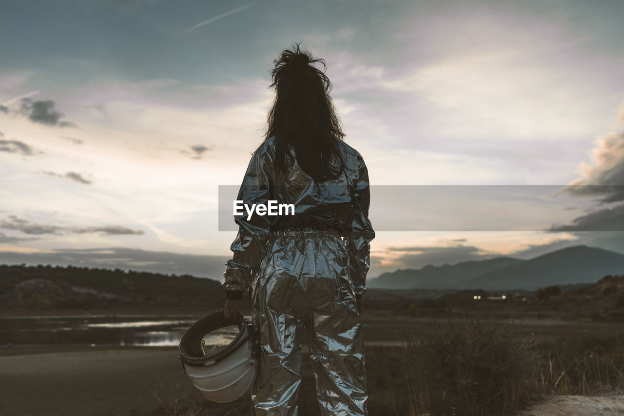 Woman astronaut holding space helmet at beach