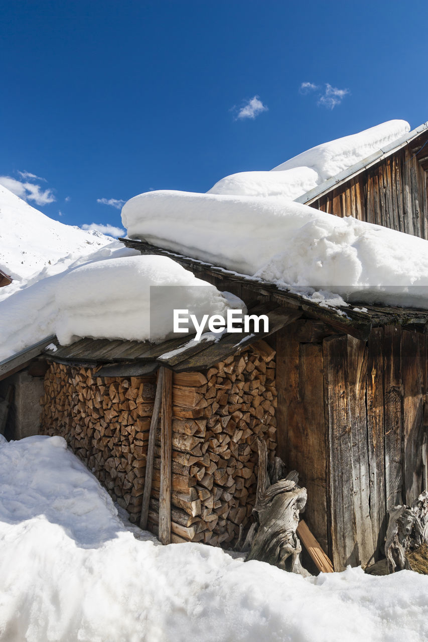 Snow covered log cabin against blue sky