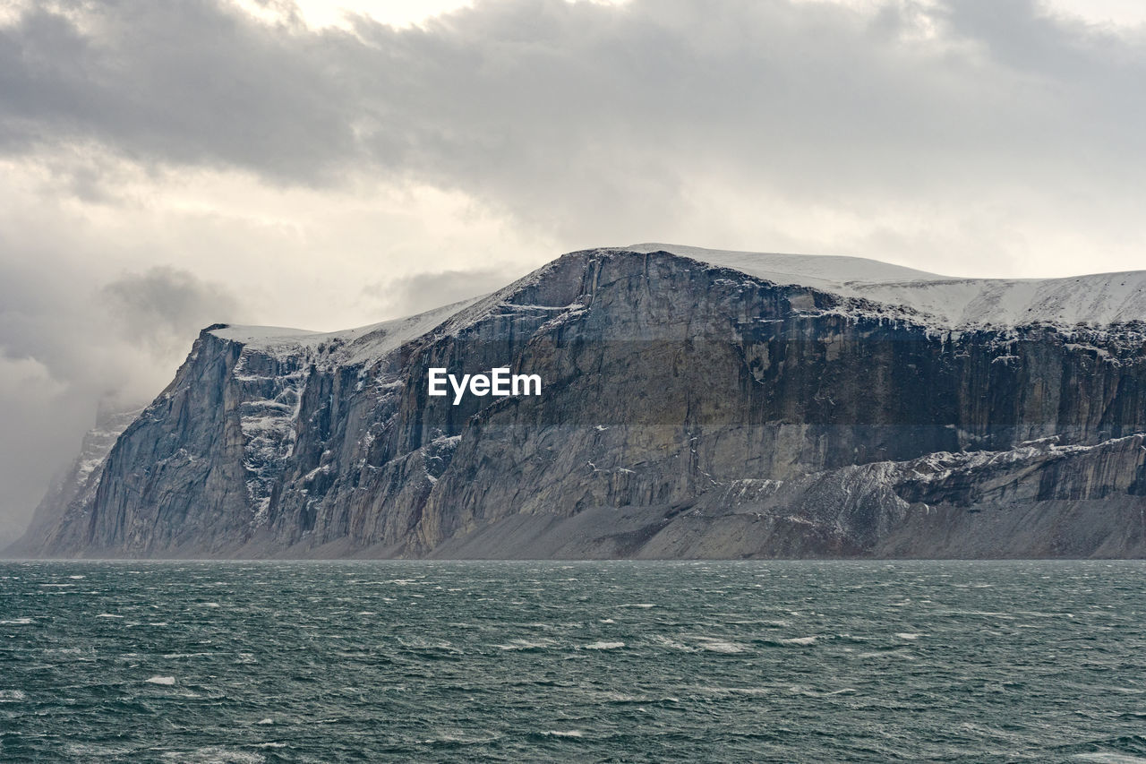 High cliffs under dramatic clouds in the sam ford fjord on baffin island in nunavut, canada