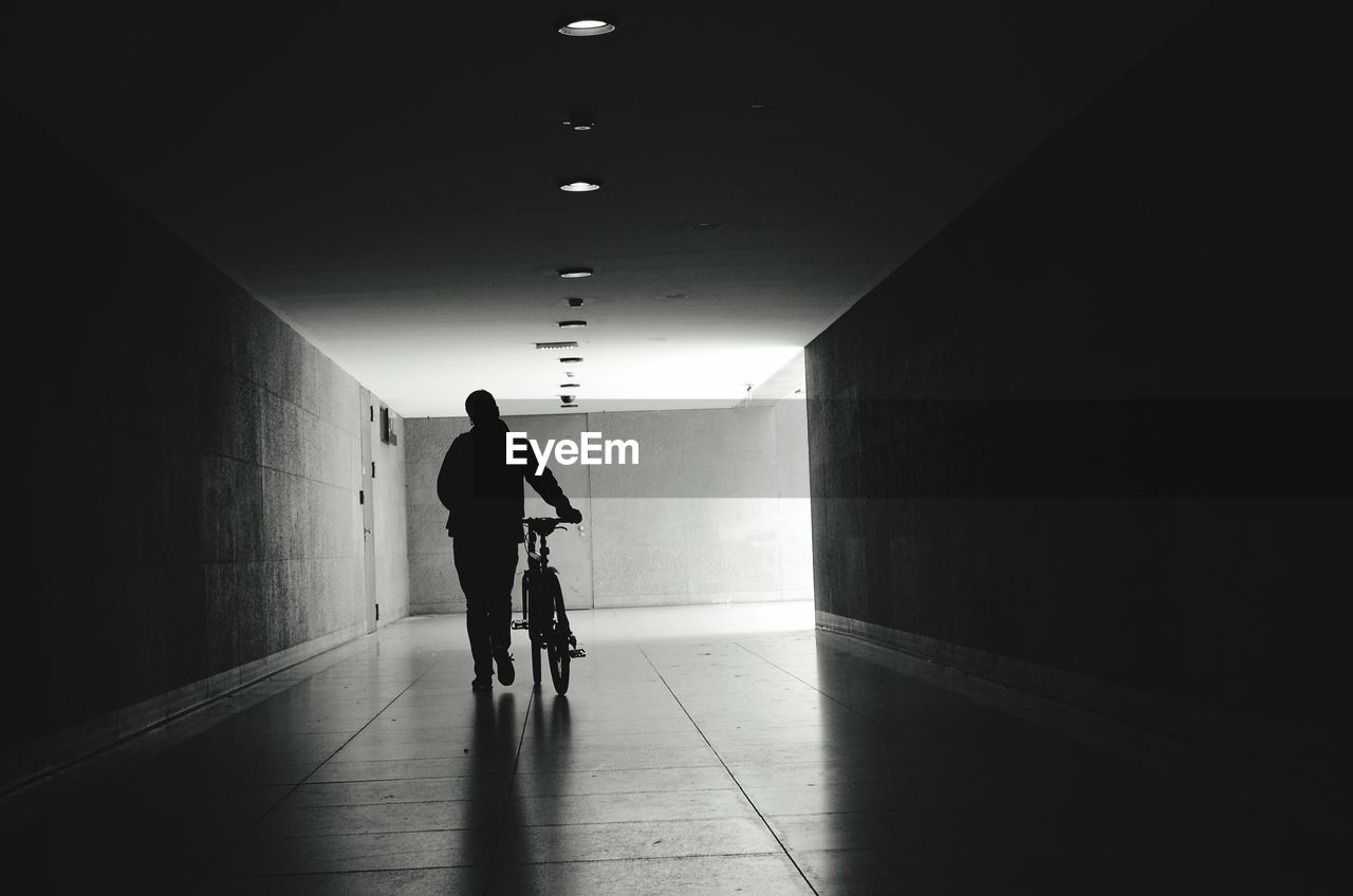 REAR VIEW OF MAN WALKING IN ILLUMINATED UNDERGROUND CORRIDOR