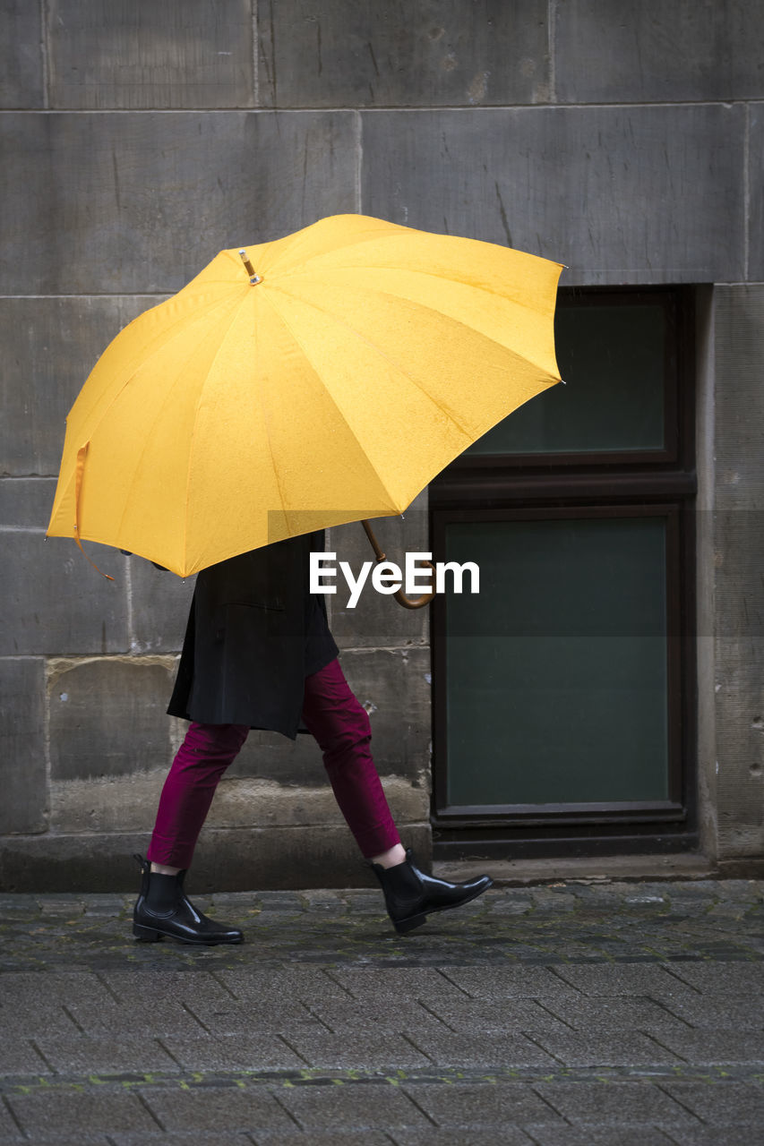 Low section of person carrying yellow umbrella on footpath during rain