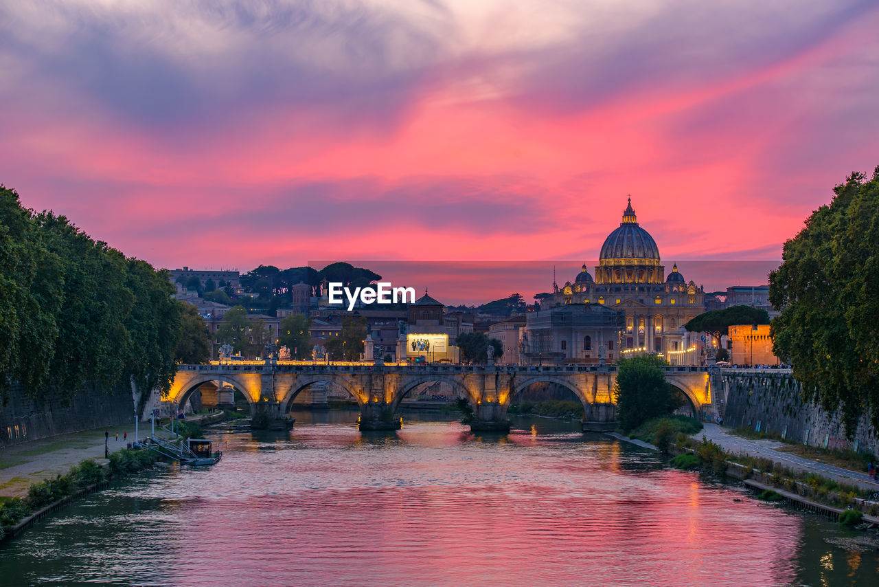 Arch bridge over river in city during sunset