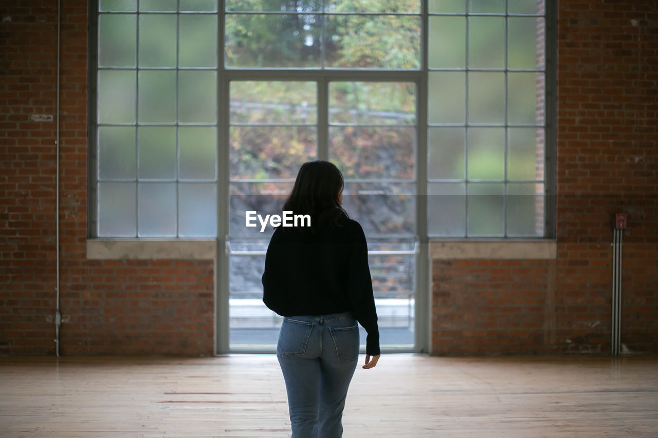 REAR VIEW OF WOMAN STANDING IN WINDOW