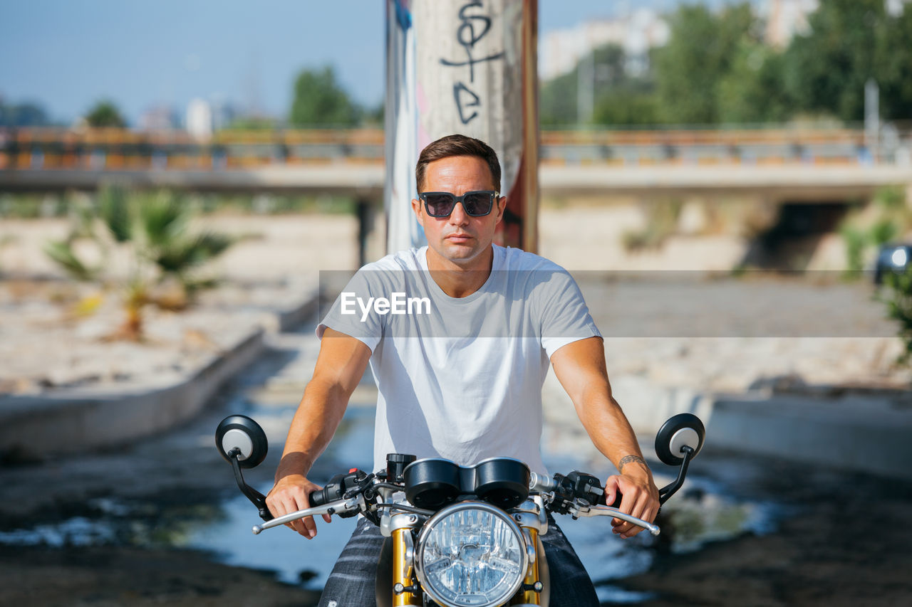 Stylish male biker sitting on modern motorcycle in urban area and looking at camera