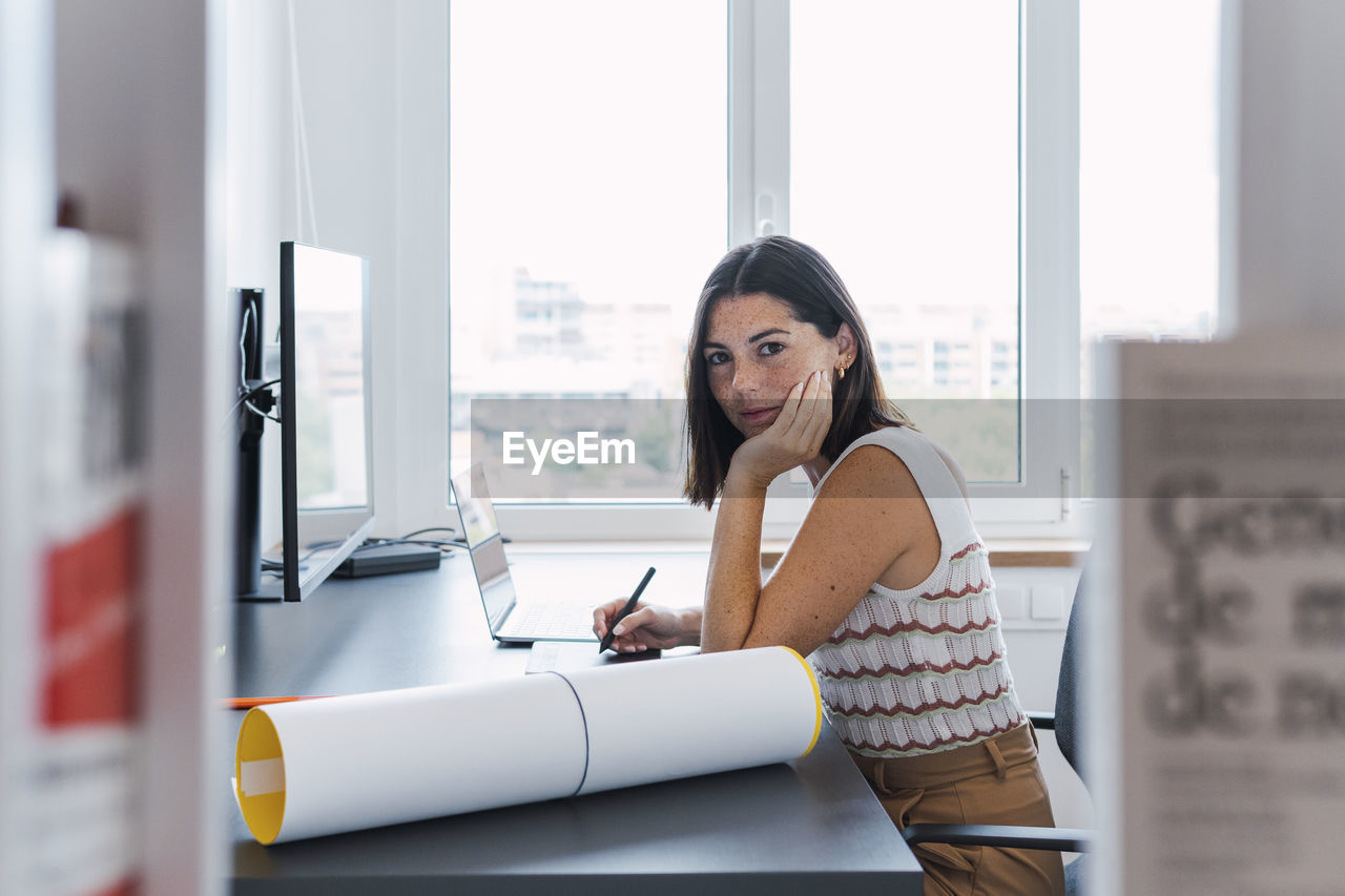 Young businesswoman sitting with hand on chin in front of desktop