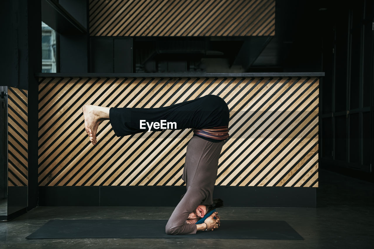 Male yoga instructor doing headstand in exercise room