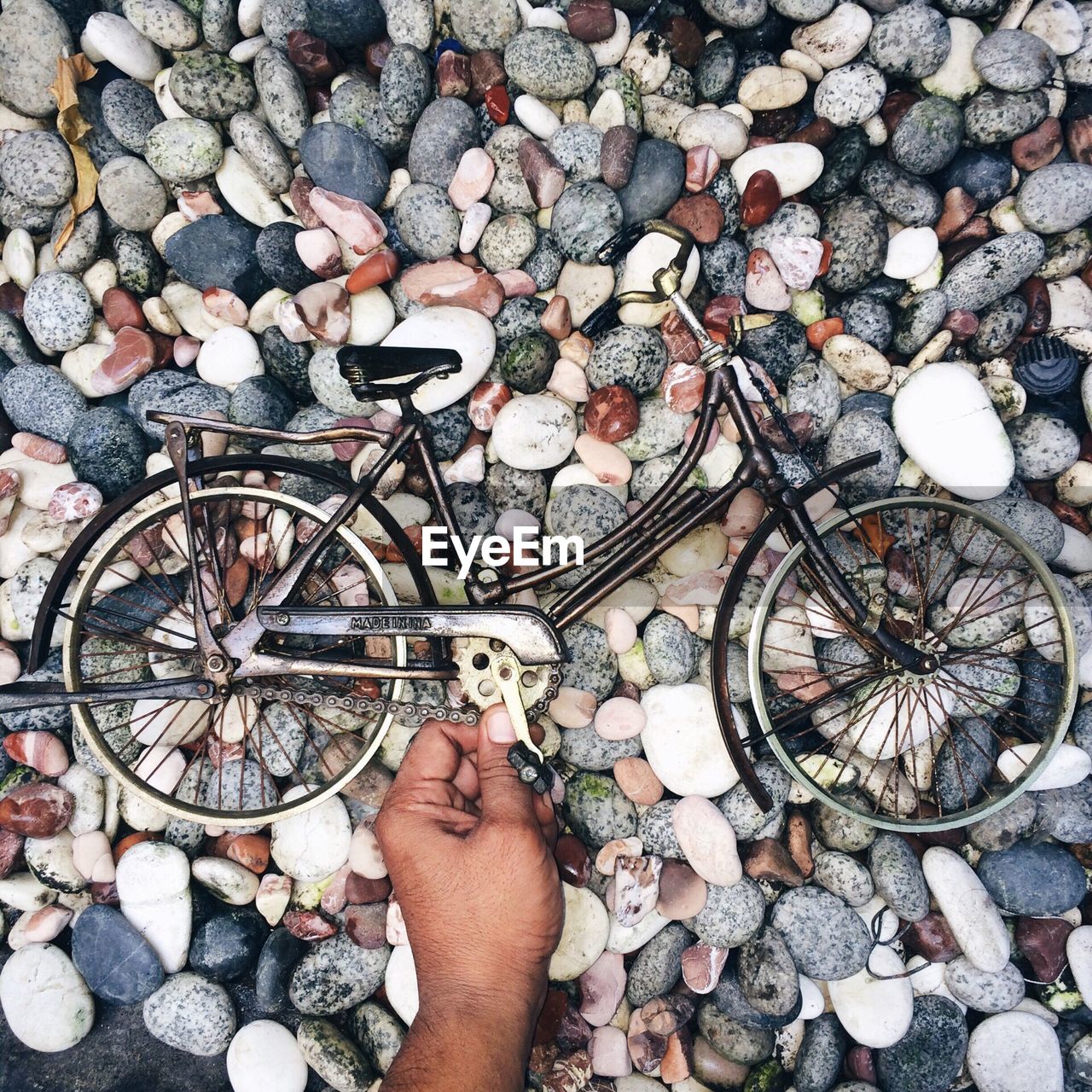 Cropped hand holding toy bicycle on pebbles